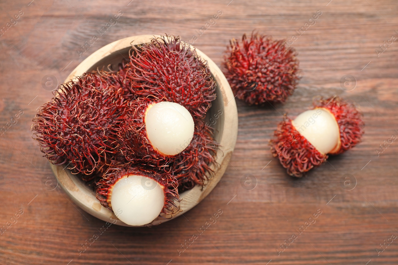 Photo of Delicious ripe rambutans in bowl on wooden table, top view