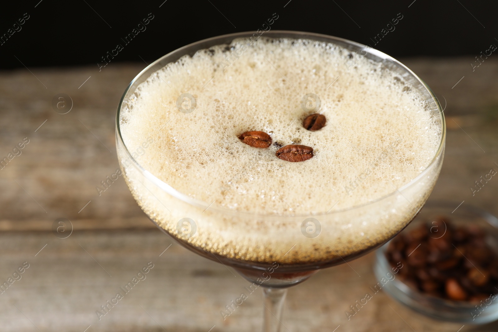 Photo of Delicious espresso martini with coffee beans in glass on blurred background, closeup