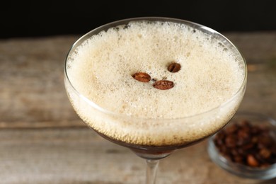 Photo of Delicious espresso martini with coffee beans in glass on blurred background, closeup