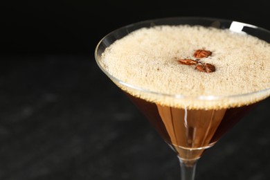 Photo of Delicious espresso martini with coffee beans in glass on blurred black background, closeup. Space for text