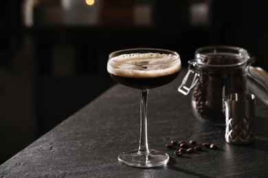 Photo of Glass with delicious espresso martini and coffee beans on dark table in bar. Space for text