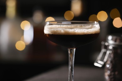 Photo of Delicious espresso martini in glass against blurred lights, closeup. Space for text