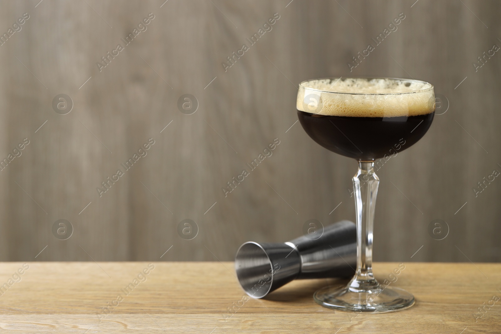 Photo of Delicious espresso martini with coffee beans in glass and jigger on wooden table. Space for text