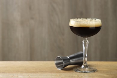 Photo of Delicious espresso martini with coffee beans in glass and jigger on wooden table. Space for text