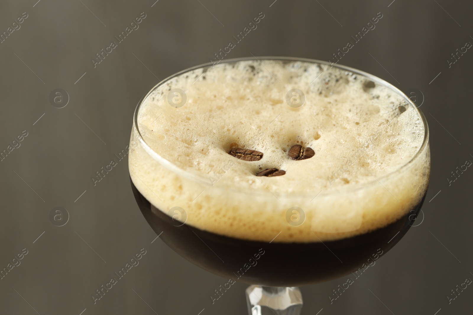 Photo of Delicious espresso martini with coffee beans in glass on blurred background, closeup