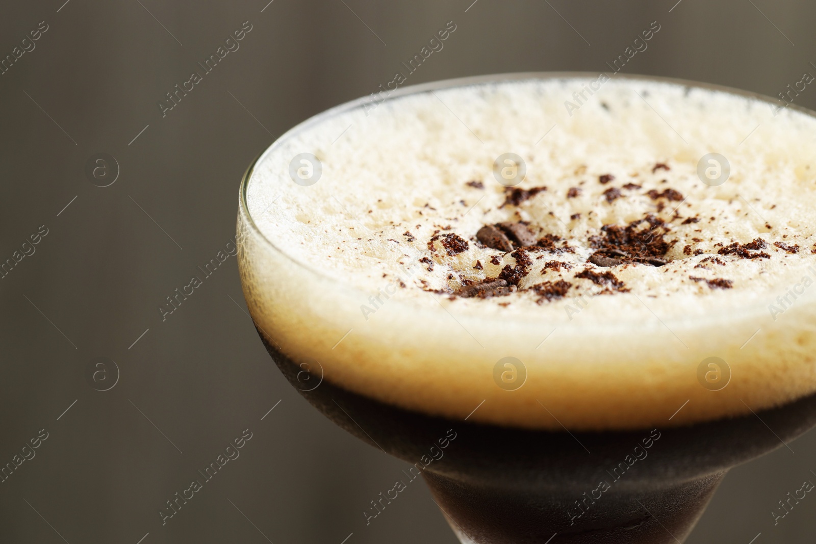 Photo of Delicious espresso martini with coffee beans in glass on blurred background, closeup