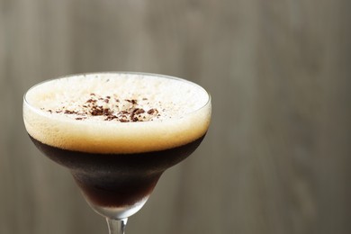 Photo of Delicious espresso martini with coffee beans in glass on blurred background, closeup. Space for text