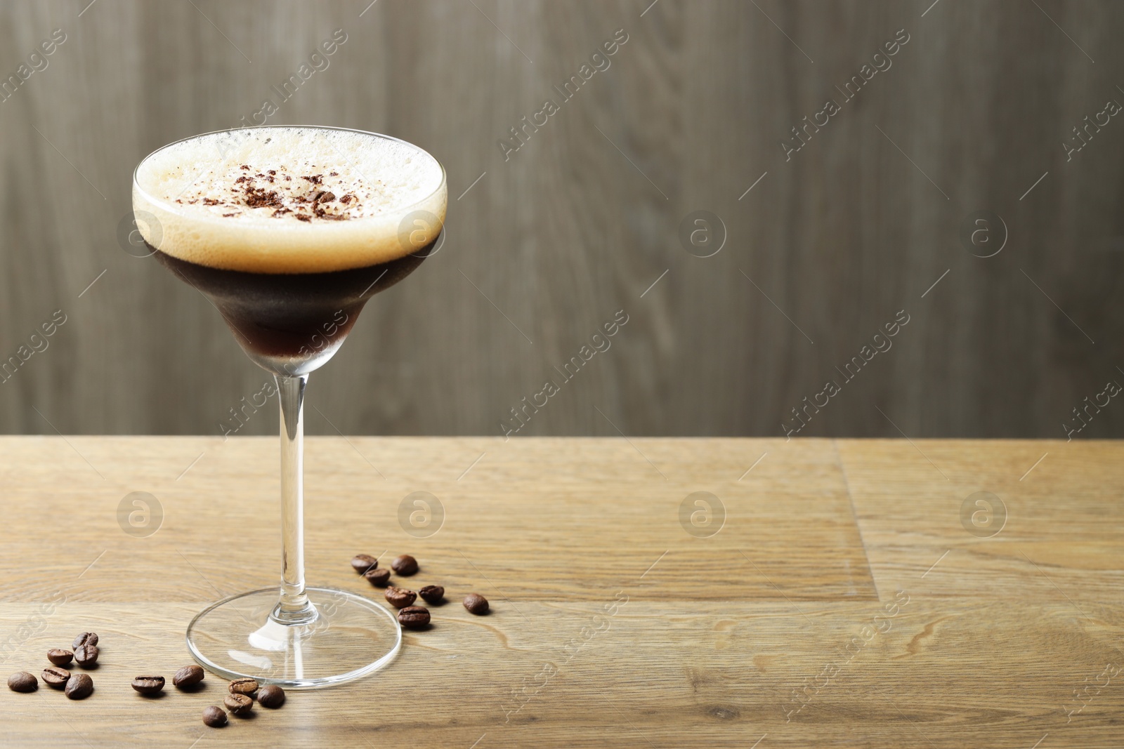 Photo of Delicious espresso martini in glass and coffee beans on wooden table. Space for text