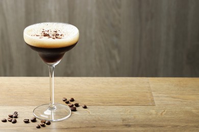 Photo of Delicious espresso martini in glass and coffee beans on wooden table. Space for text