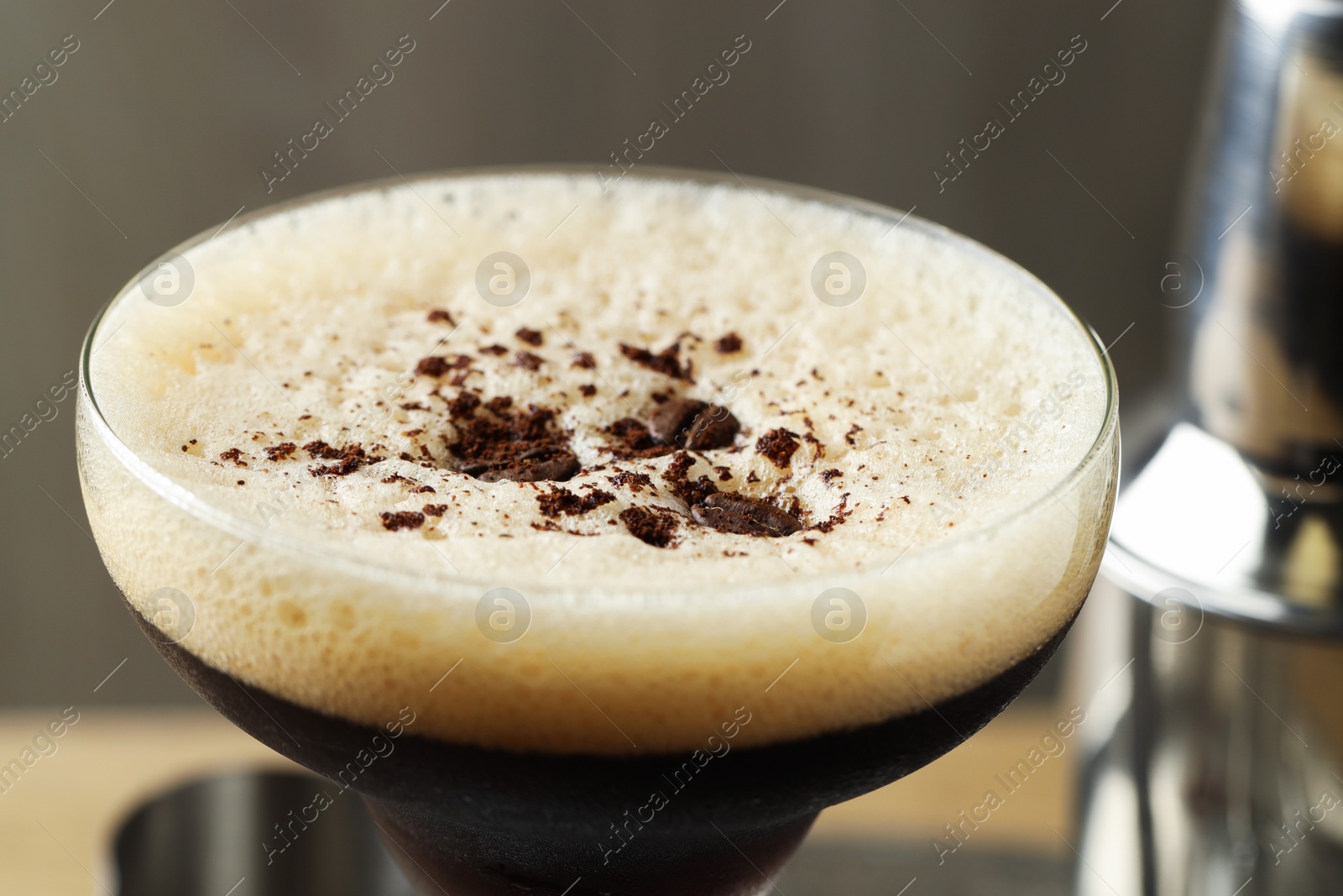 Photo of Delicious espresso martini with coffee beans in glass on blurred background, closeup