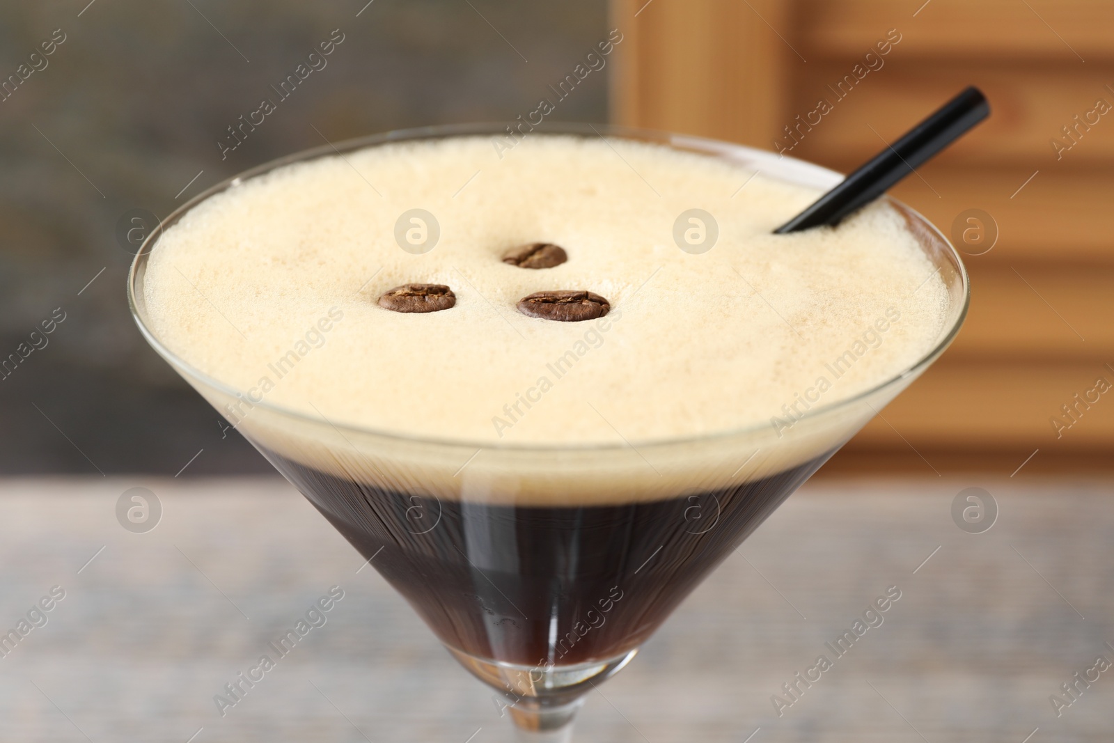 Photo of Delicious espresso martini with coffee beans in glass against blurred background, closeup