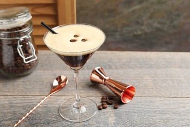 Photo of Delicious espresso martini with coffee beans in glass and bartender equipment on wooden table