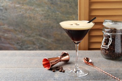 Photo of Delicious espresso martini with coffee beans in glass and bartender equipment on wooden table, space for text