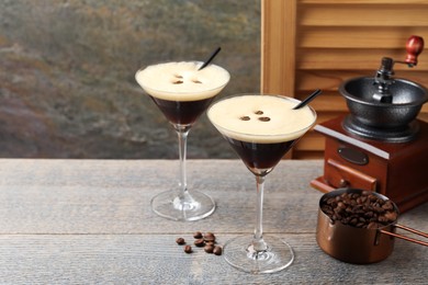 Photo of Glasses of delicious espresso martini, manual coffee grinder and beans on wooden table