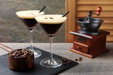 Photo of Glasses of delicious espresso martini, manual coffee grinder and beans on wooden table