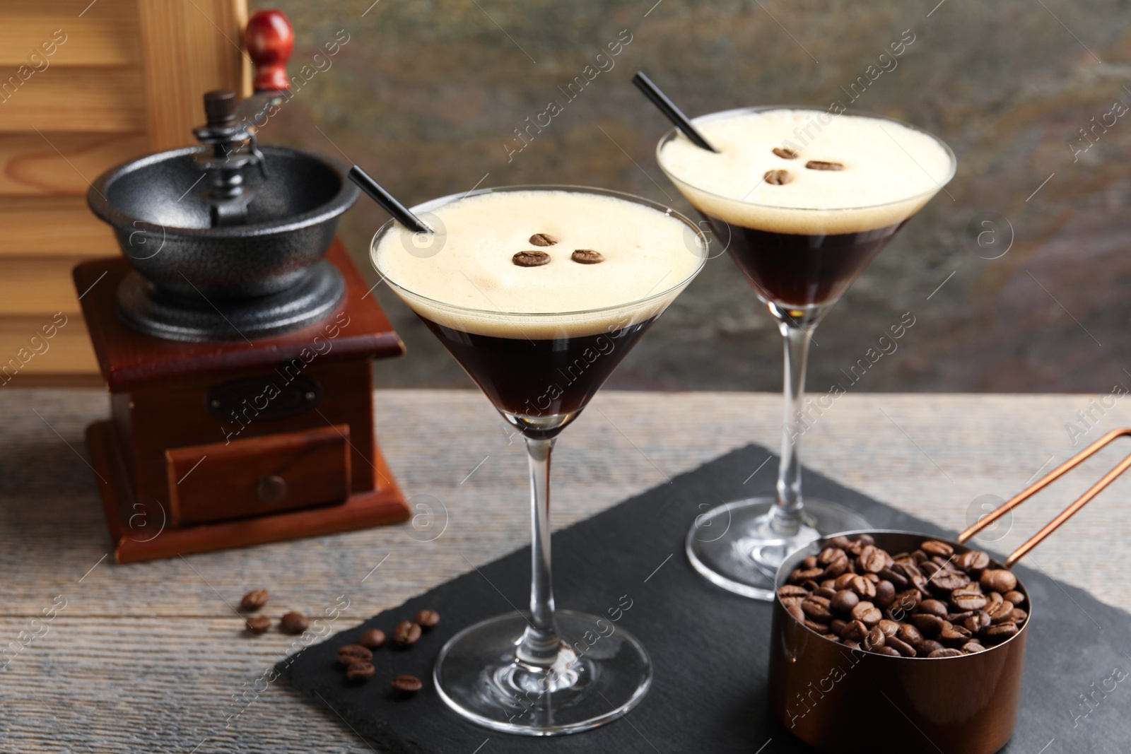 Photo of Glasses of delicious espresso martini, manual coffee grinder and beans on wooden table