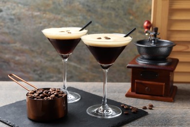 Photo of Glasses of delicious espresso martini, manual coffee grinder and beans on wooden table