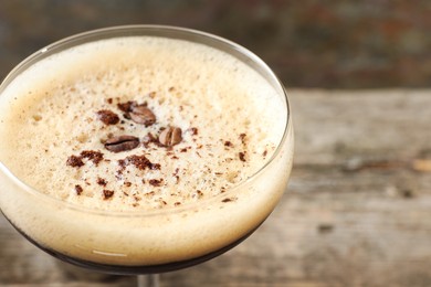 Photo of Delicious espresso martini with coffee beans in glass against blurred background, closeup