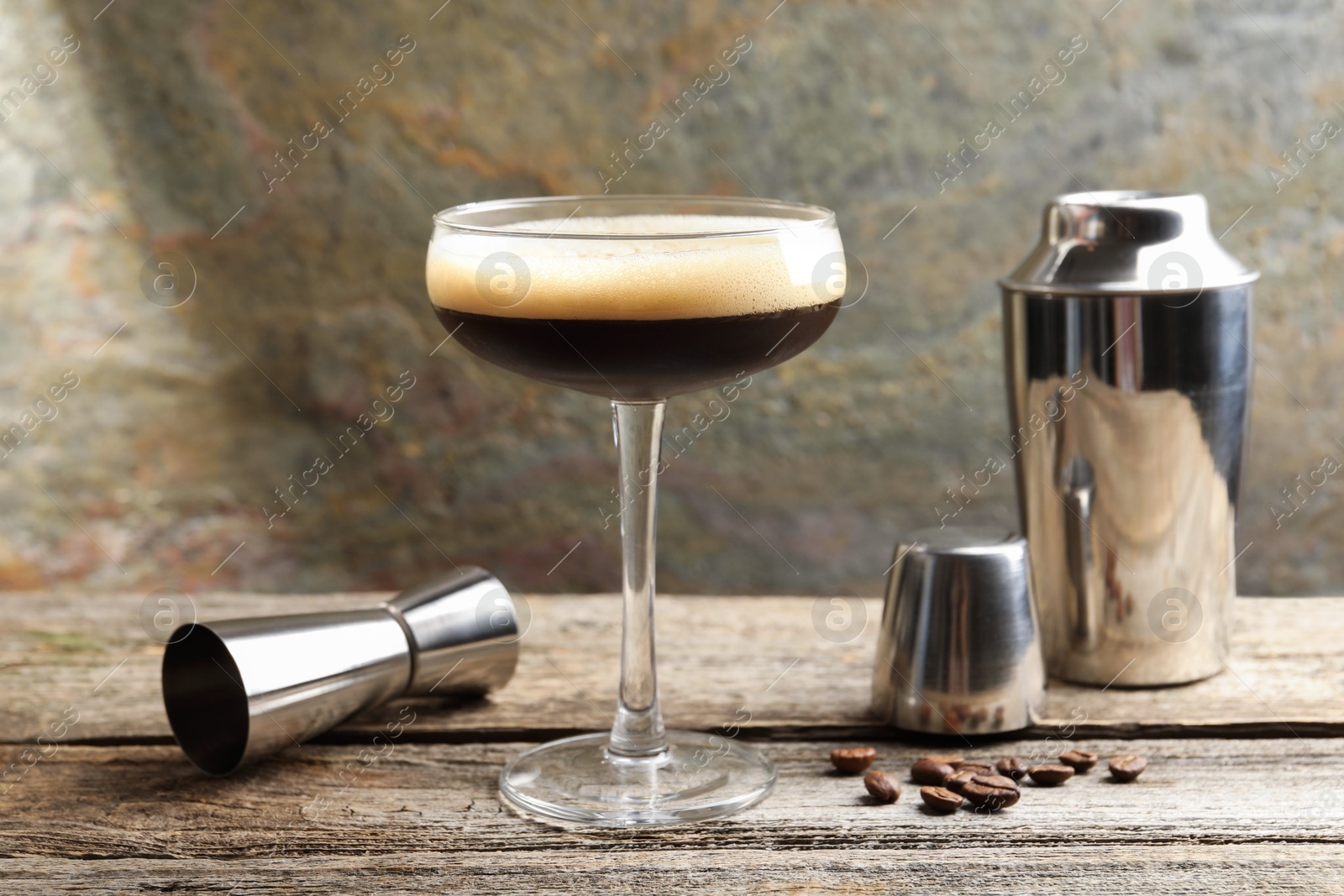 Photo of Delicious espresso martini with coffee beans in glass and bartender equipment on wooden table