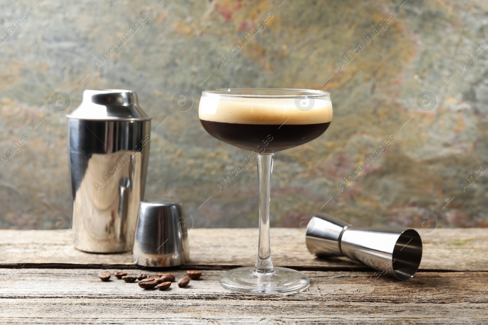 Photo of Delicious espresso martini with coffee beans in glass and bartender equipment on wooden table