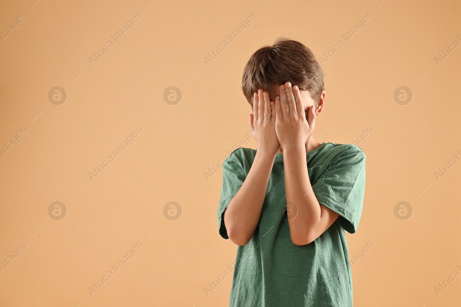 Photo of Scared little boy covering face with hands on beige background. Space for text