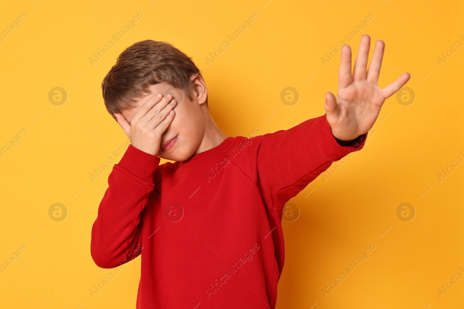 Photo of Scared little boy covering eyes on orange background