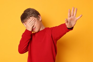 Photo of Scared little boy covering eyes on orange background