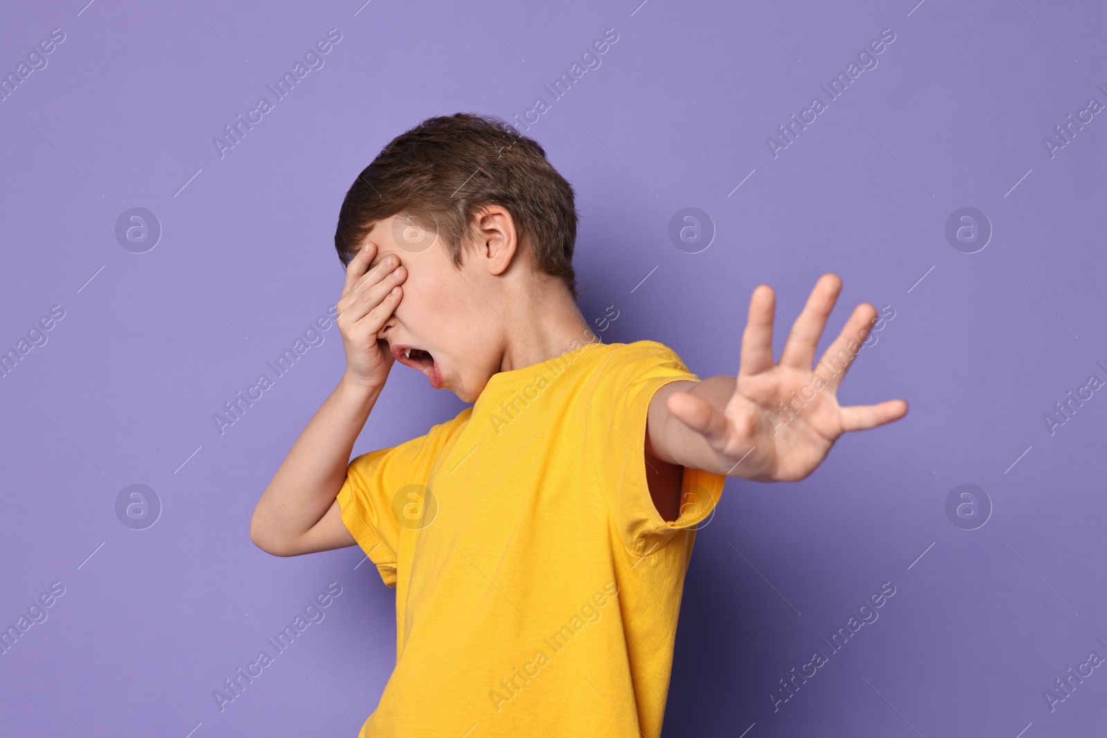 Photo of Scared little boy covering eyes on violet background