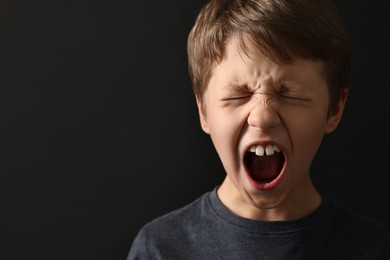 Photo of Scared little boy screaming on black background. Space for text