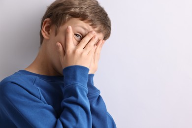 Photo of Scared little boy hiding on light background. Space for text