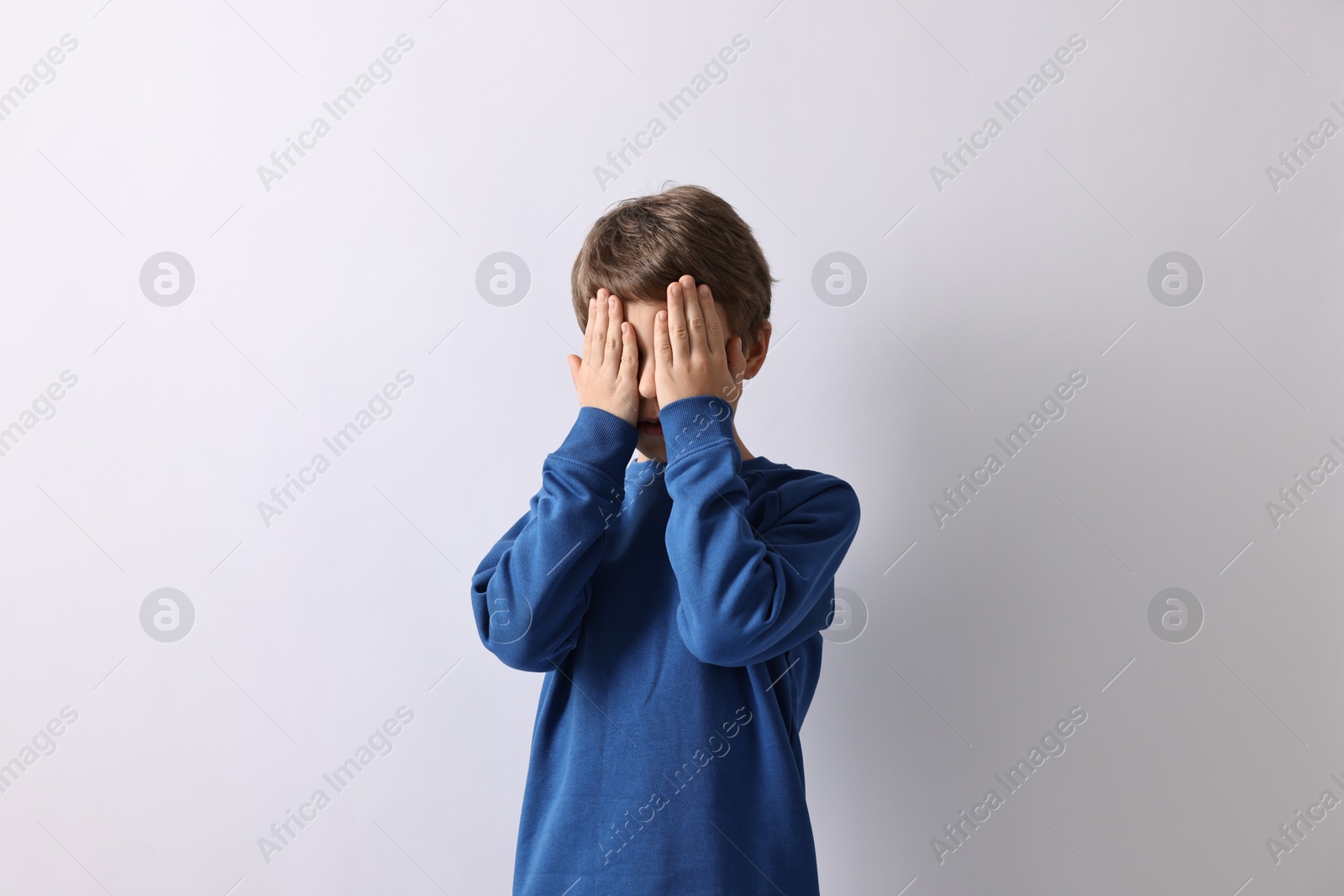 Photo of Scared little boy covering face with hands on light background