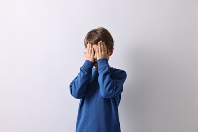 Photo of Scared little boy covering face with hands on light background