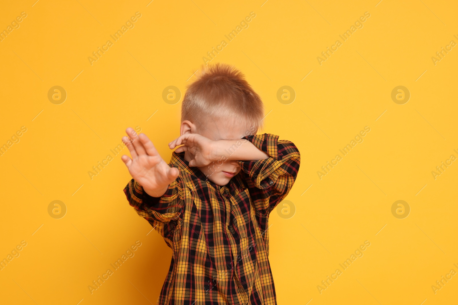 Photo of Scared little boy covering eyes on orange background