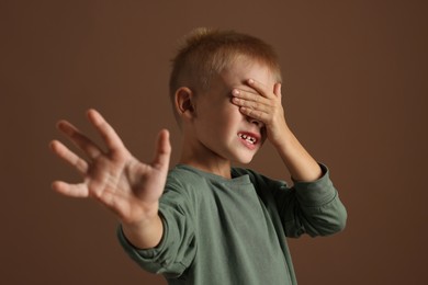 Photo of Scared little boy covering face with hand on brown background