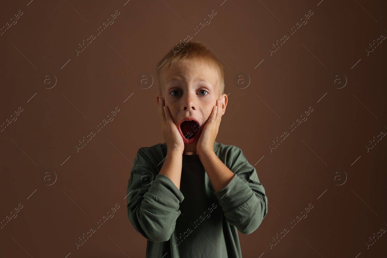 Photo of Scared little boy screaming on brown background