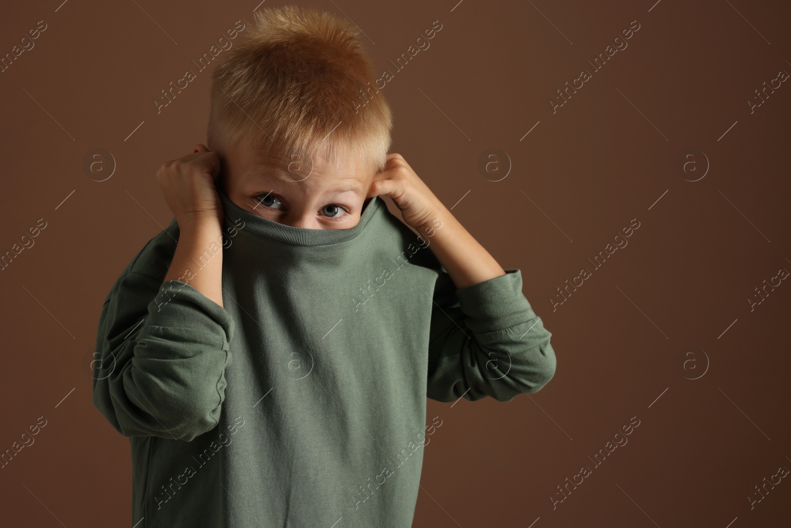 Photo of Scared little boy hiding on brown background. Space for text