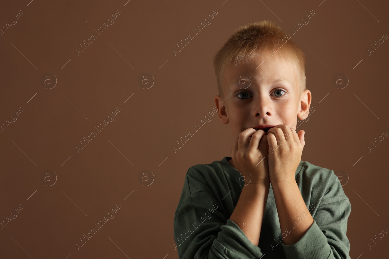 Photo of Scared little boy on brown background. Space for text