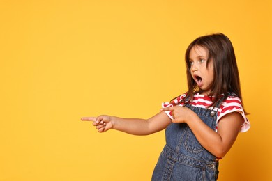 Photo of Scared little girl pointing at something on orange background. Space for text