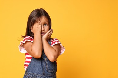 Photo of Portrait of scared little girl on orange background. Space for text