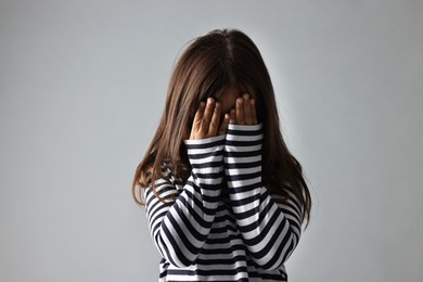 Photo of Scared little girl covering face with hands on grey background