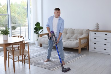 Photo of Young man cleaning floor with cordless vacuum cleaner at home