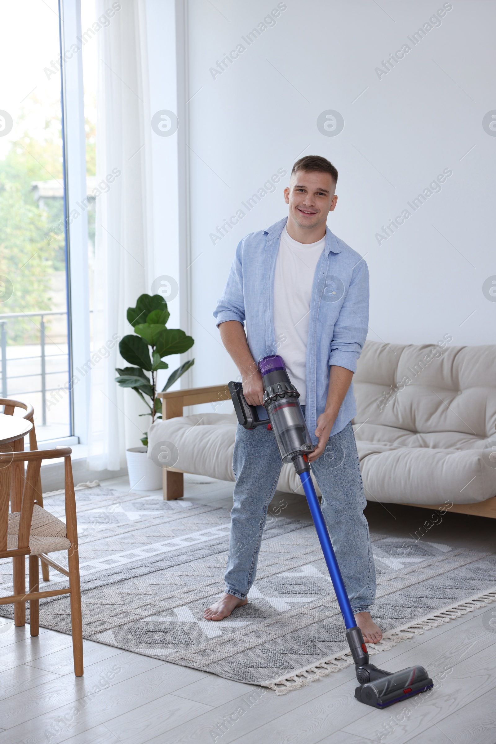 Photo of Young man cleaning floor with cordless vacuum cleaner at home