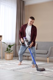 Photo of Young man cleaning rug with cordless vacuum cleaner at home