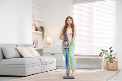 Photo of Teenage girl cleaning rug with cordless vacuum cleaner at home