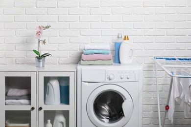 Photo of Laundry detergents and stacked clean towels on washing machine in bathroom