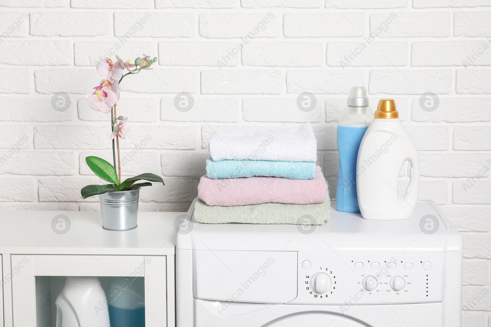 Photo of Laundry detergents and stacked clean towels on washing machine in bathroom