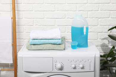 Photo of Laundry detergent, cap and stacked clean towels on washing machine in bathroom