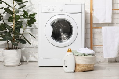 Photo of Detergent and basket with laundry near washing machine in bathroom