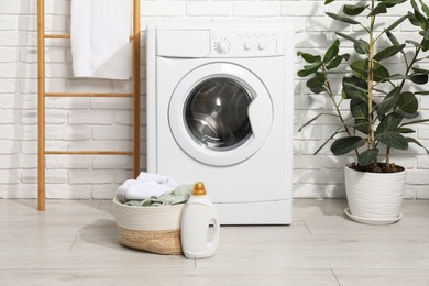 Photo of Detergent and basket with laundry near washing machine in bathroom