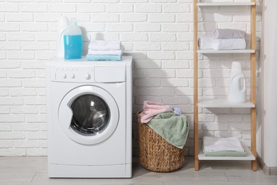 Photo of Laundry detergents and stacked clean towels on washing machine in bathroom